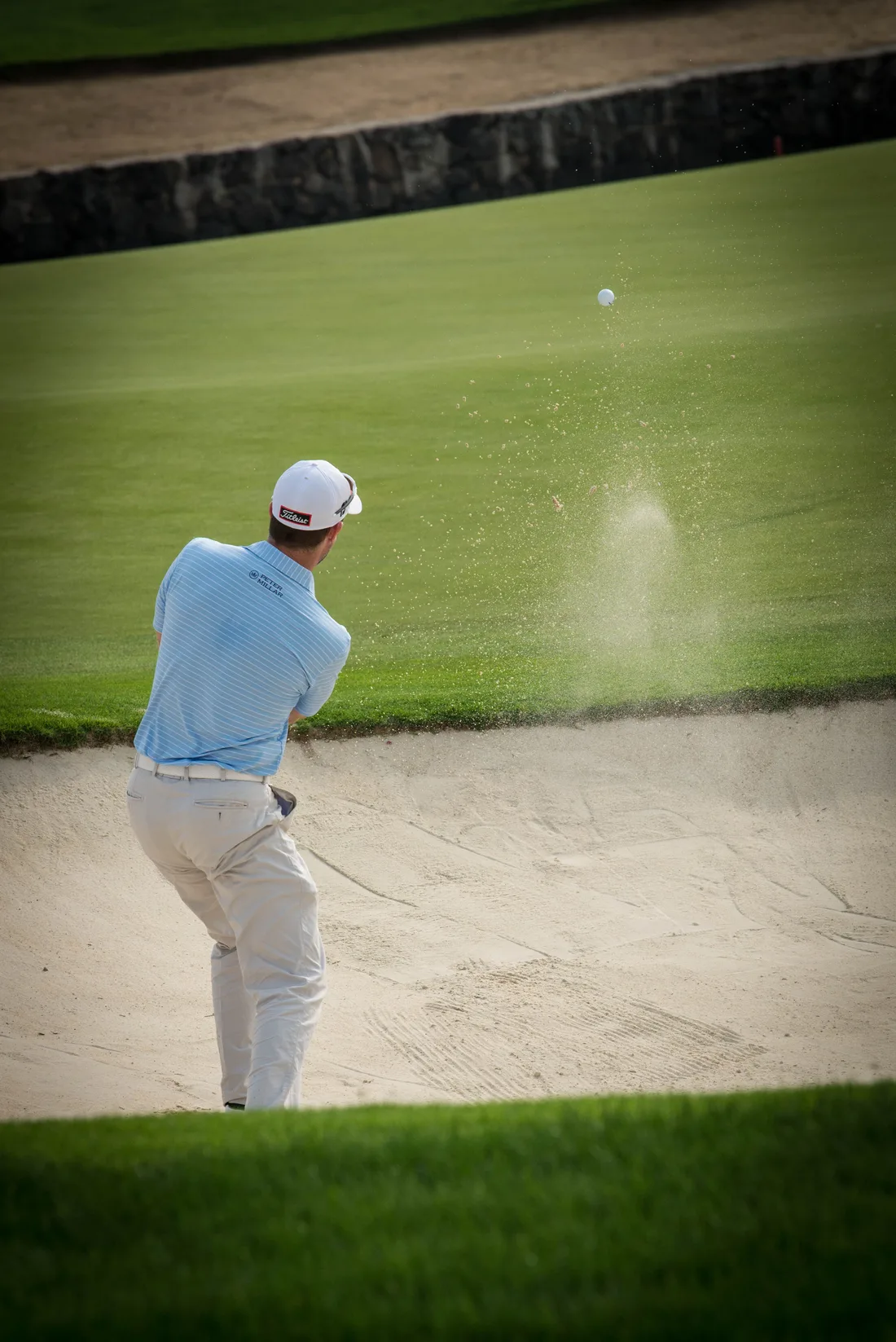 A golfer playing a shot from a greenside bunker